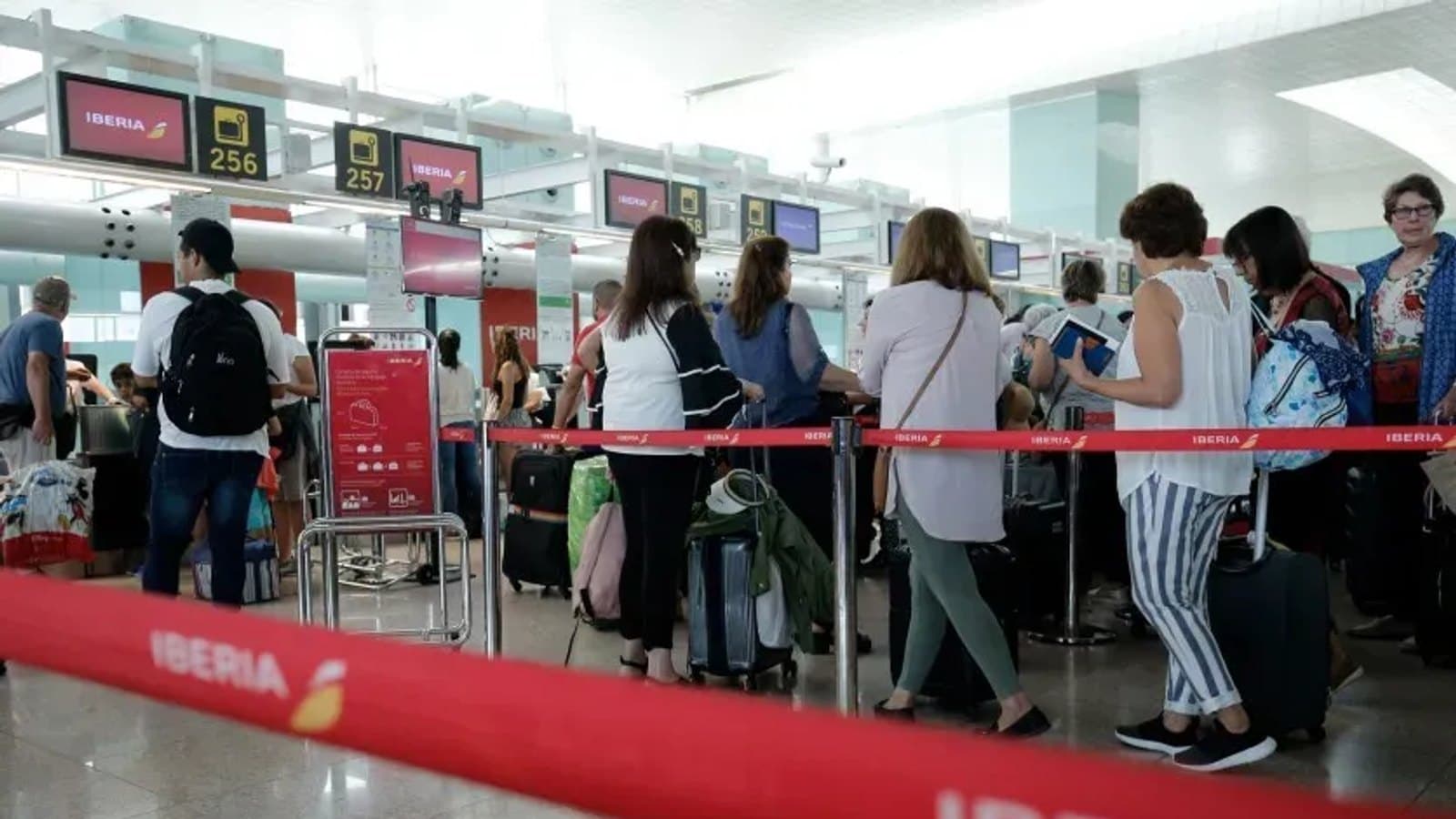 Viajeros hacen cola tras una valla roja de Iberia ante los mostradores de facturación del aeropuerto de Barcelona El Prat.